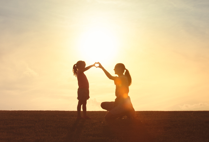 woman and daughter making heart shape against a beautiful sunset.